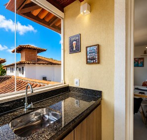A kitchen with a sink, a window overlooking a tiled roof, and two framed posters on the wall.