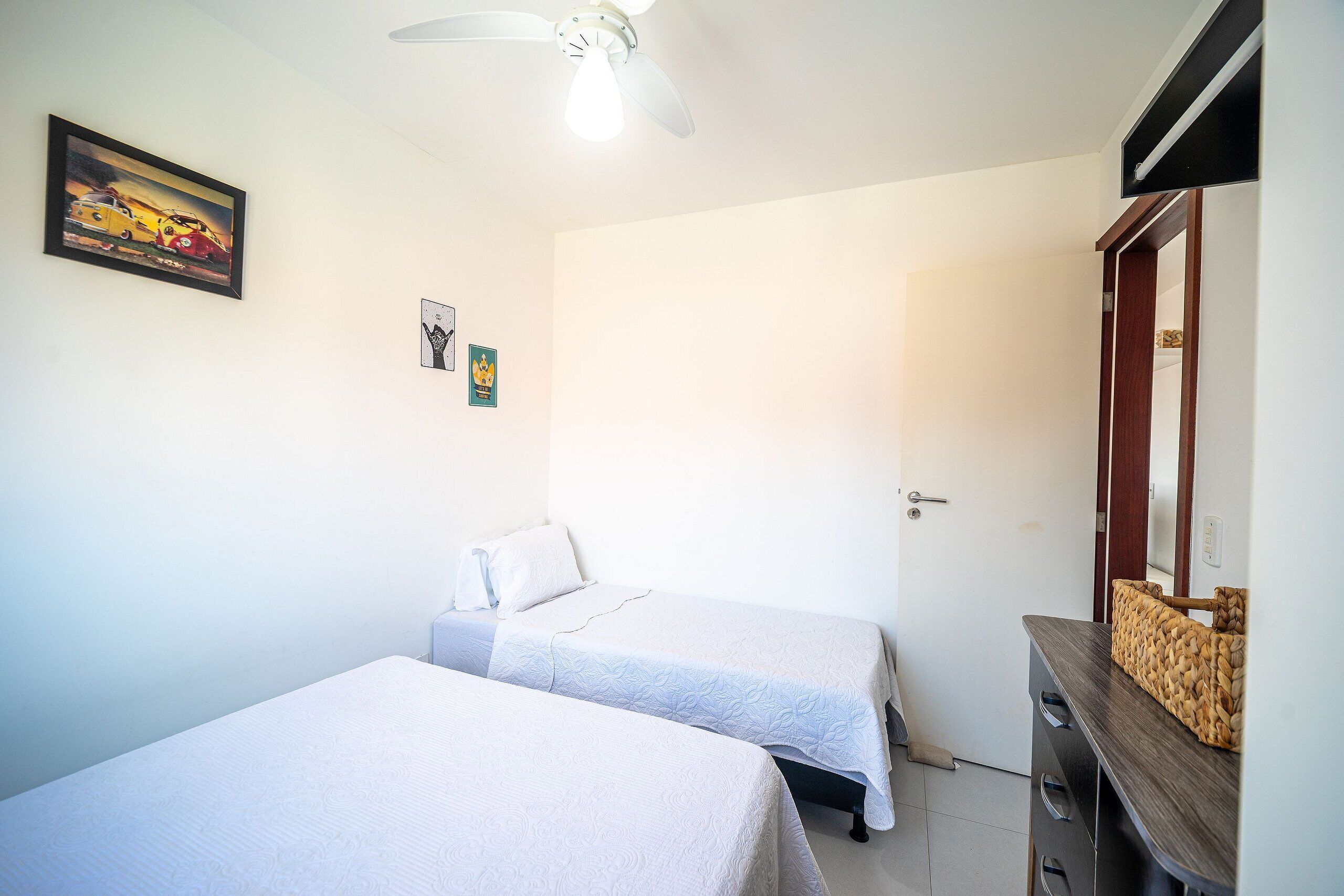 Une chambre avec deux lits, un ventilateur de plafond, une commode et un tableau au mur.