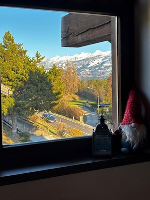 Blick aus dem Fenster auf eine Straße mit einem Berg im Hintergrund, eine Lampe und eine Gartenzwergfigur auf der Fensterbank.