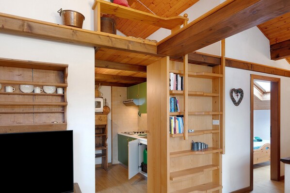 A compact kitchen with a stove, microwave, and wooden shelves.
