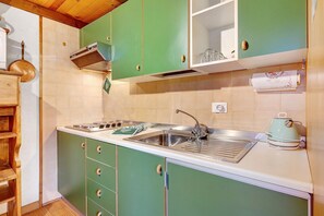 A kitchen with green cabinets, a stainless steel sink, and a kettle.