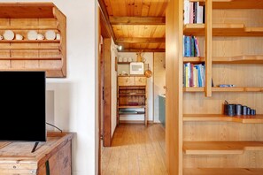 A wooden interior with a television on a wooden stand, a microwave, and shelves with books and kitchen items.