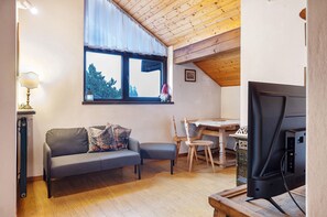 A cozy room with a wooden ceiling, a gray sofa, a wooden dining table, and a television.