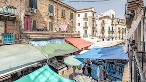 Une rue étroite bordée d’étals de marché en plein air, protégés par des auvents, de bâtiments dotés de balcons et de climatiseurs.