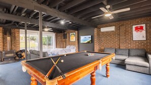 A pool table in a room with a brick wall, a ceiling fan, and a large window. - The Wreck Room, 6 Flannel Flower Fairway - fantastic house filled with activities for all (Shoal Bay)