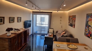 A modern living room with a flat-screen TV, a sofa, a dining table, and a cabinet.