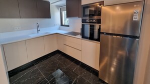 A modern kitchen with white cabinets, a stainless steel refrigerator, an oven, and a microwave.