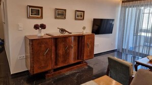 A modern living room with a wooden cabinet, a flat-screen TV, and a dining area with a table and chairs.