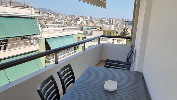 A balcony with a table and chairs, overlooking a cityscape.