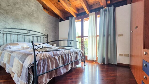 Un dormitorio con estructura de cama metálica, suelo de madera y un ventanal con cortinas.