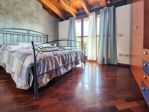 Ein Schlafzimmer mit einem Metallbettgestell, Holzboden und einem großen Fenster mit Vorhängen.