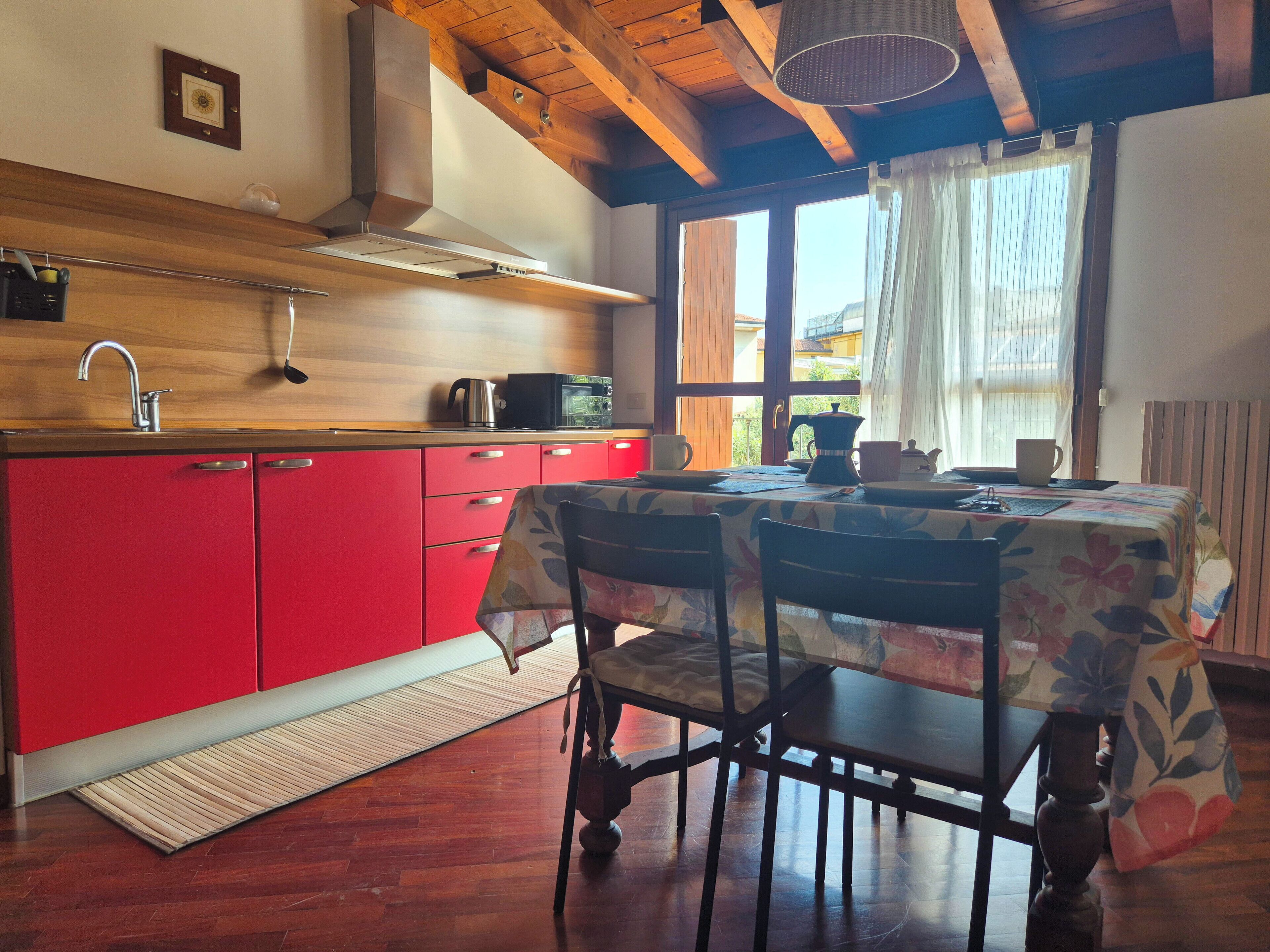 Cozinha com armários vermelhos, bancada de madeira e janela com cortinas.