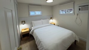 Ein Schlafzimmer mit einem Bett, zwei Nachttischen, einem Fenster und einer Deckenleuchte.
