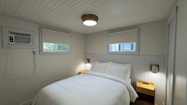 Ein Schlafzimmer mit einem Bett, zwei Nachttischen, einer Wandheizung und zwei Fenstern.