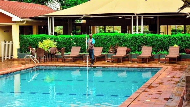 A swimming pool with lounge chairs and a person cleaning it. - Theta Country Resort (Juja)