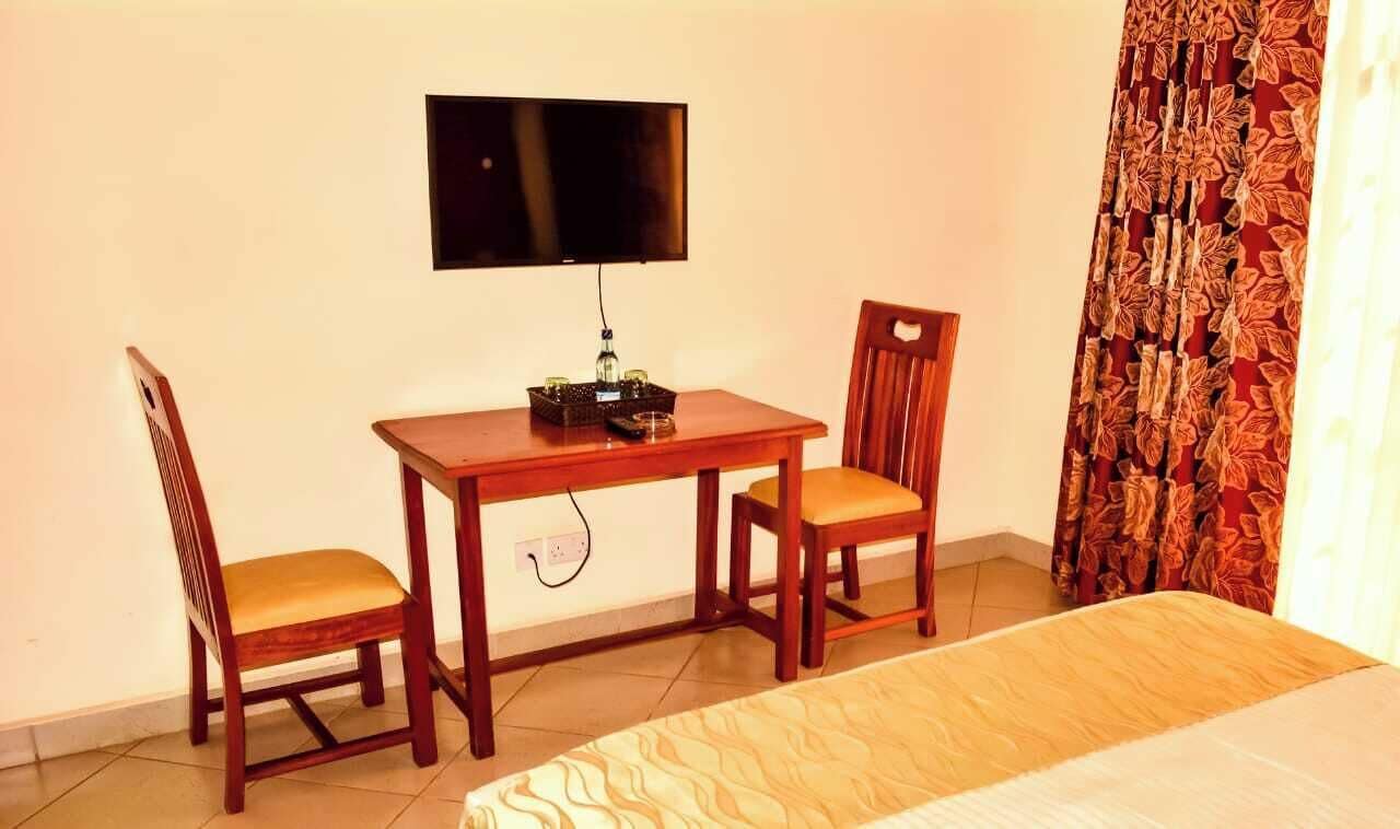 Une pièce comprenant un lit, un bureau avec deux chaises, un téléviseur fixé au mur et un rideau à motifs.