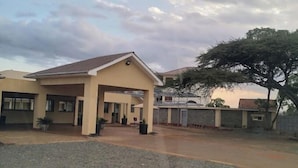A two-story building with a covered entrance and a large tree in front. - Theta Country Resort (Juja)