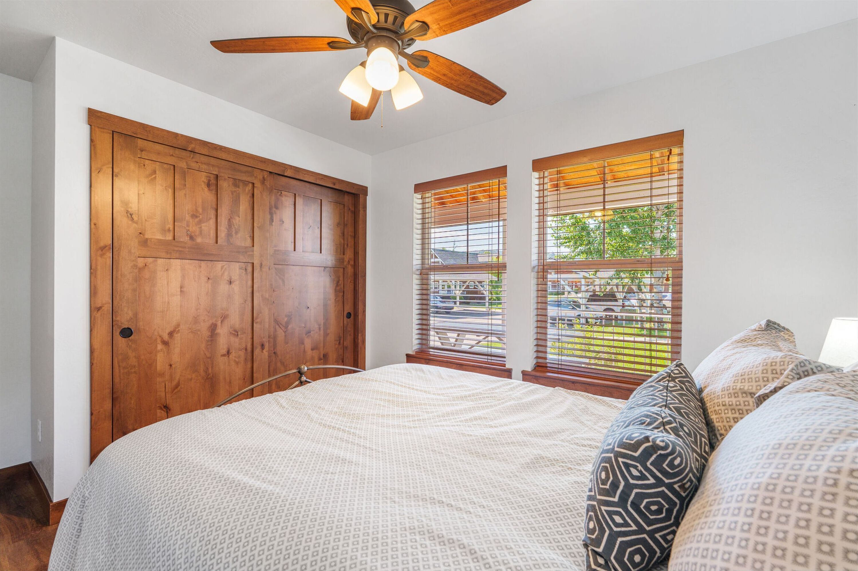 A bedroom with a large bed, wooden wardrobe, and a ceiling fan.