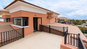 Un edificio residencial moderno con techo plano, balcón y entrada protegida por un portón.