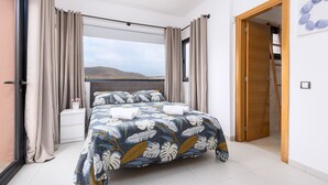Un dormitorio con una cama grande, cortinas color beige y vistas a las montañas, además de una puerta de madera.