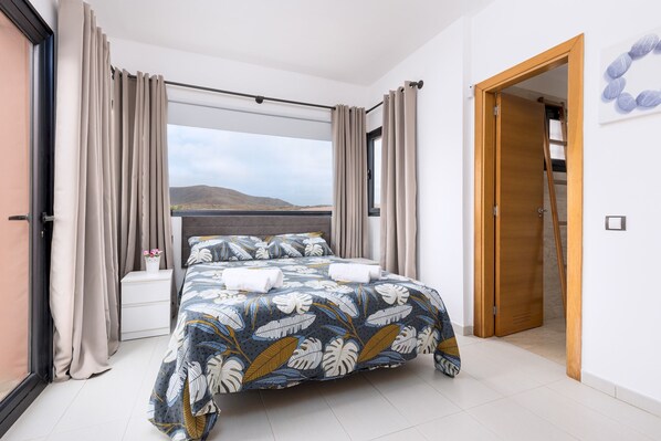 Un dormitorio con una cama grande, cortinas color beige y vistas a las montañas, además de una puerta de madera.