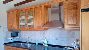 A kitchen with wooden cabinets, a stainless steel range hood, a microwave, and a sink.