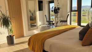 A modern bedroom with a large bed, a dining area with a view, and a potted plant. - SUPERIOR ACCOMMODATION WITH BREATHTAKING COUNTRYSIDE VIEWS (Glanton)