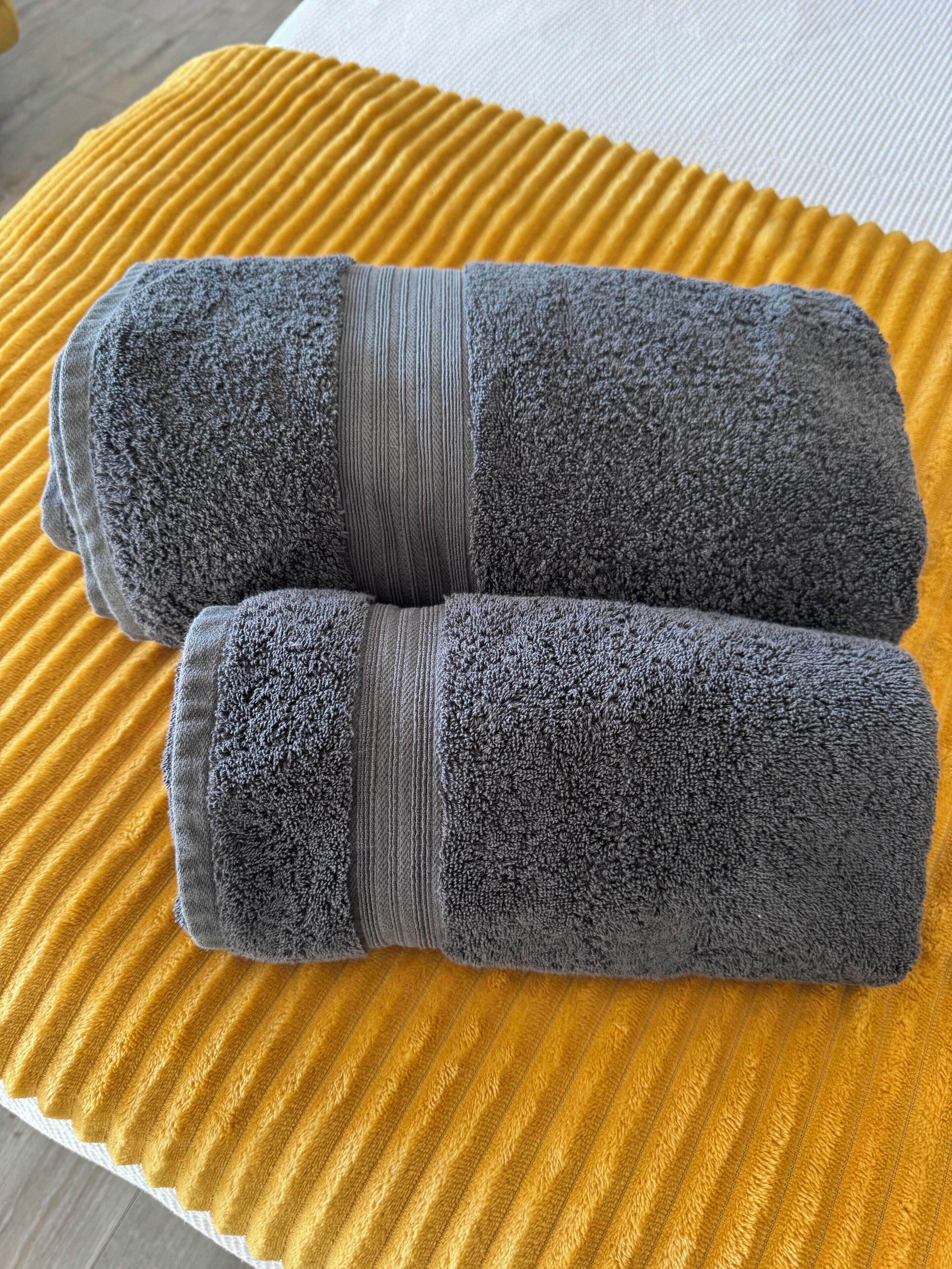 A pair of rolled gray towels on a textured yellow rug.