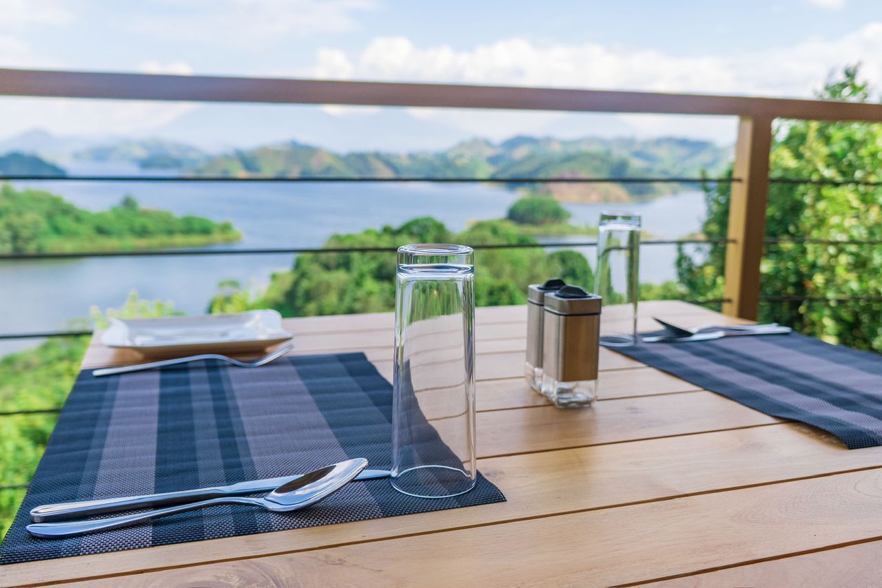 A wooden table with a placemat, a glass water bottle, a metal container, and a spoon.