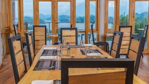 A dining area with a wooden table set for six, large windows offering a view of a lake and mountains. - NDERE  ECHIFUUHA RESORT (Kisoro)