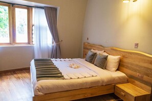 A neatly made bed with a wooden headboard, a bedside table, and a window with curtains. - NDERE  ECHIFUUHA RESORT (Kisoro)