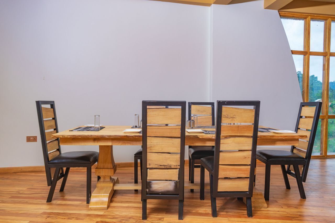 Een eethoek met een houten tafel en stoelen, een raam met uitzicht op groen en een witte muur.