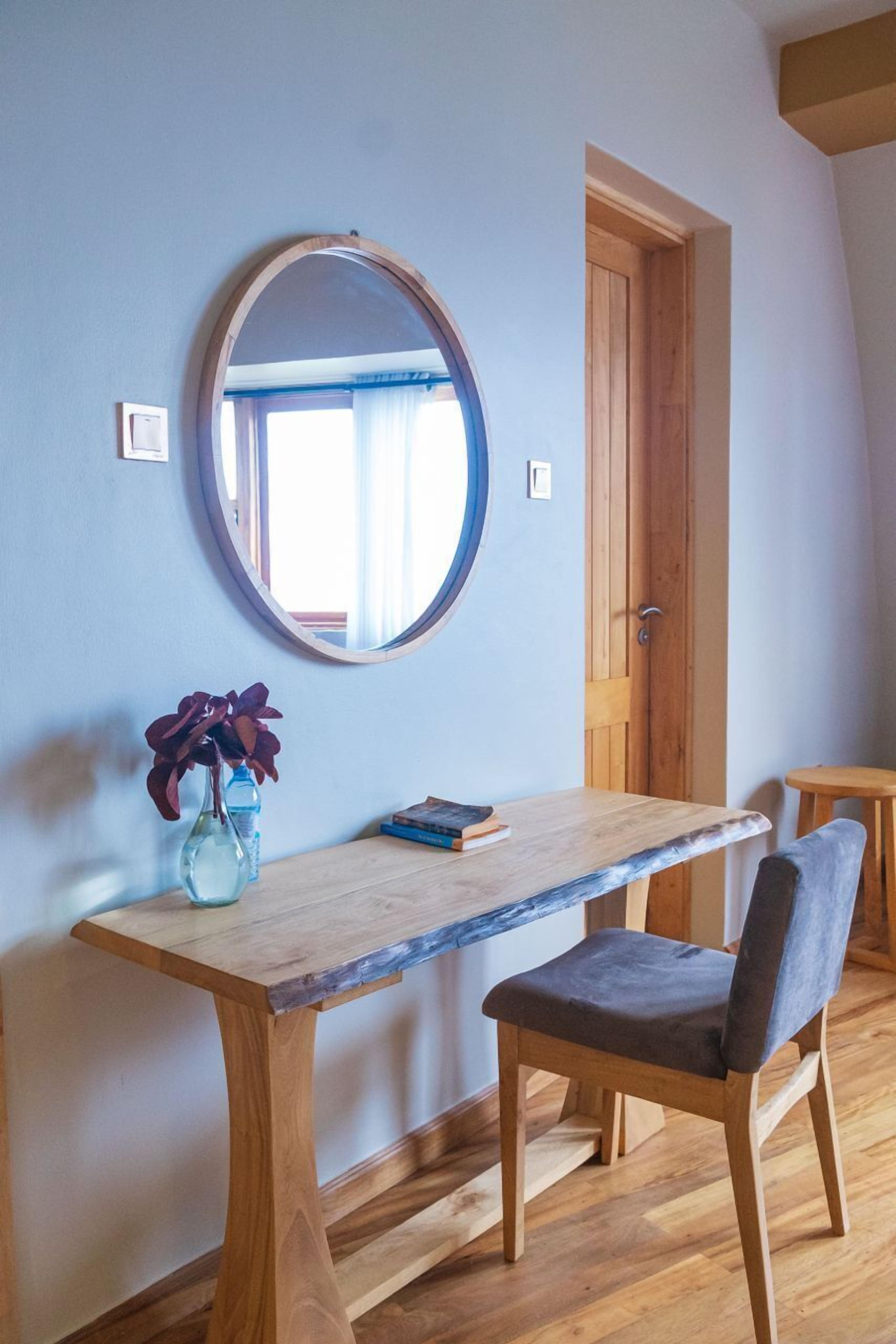Una mesa de comedor de madera con una silla, un espejo redondo en la pared y una puerta de madera al fondo.