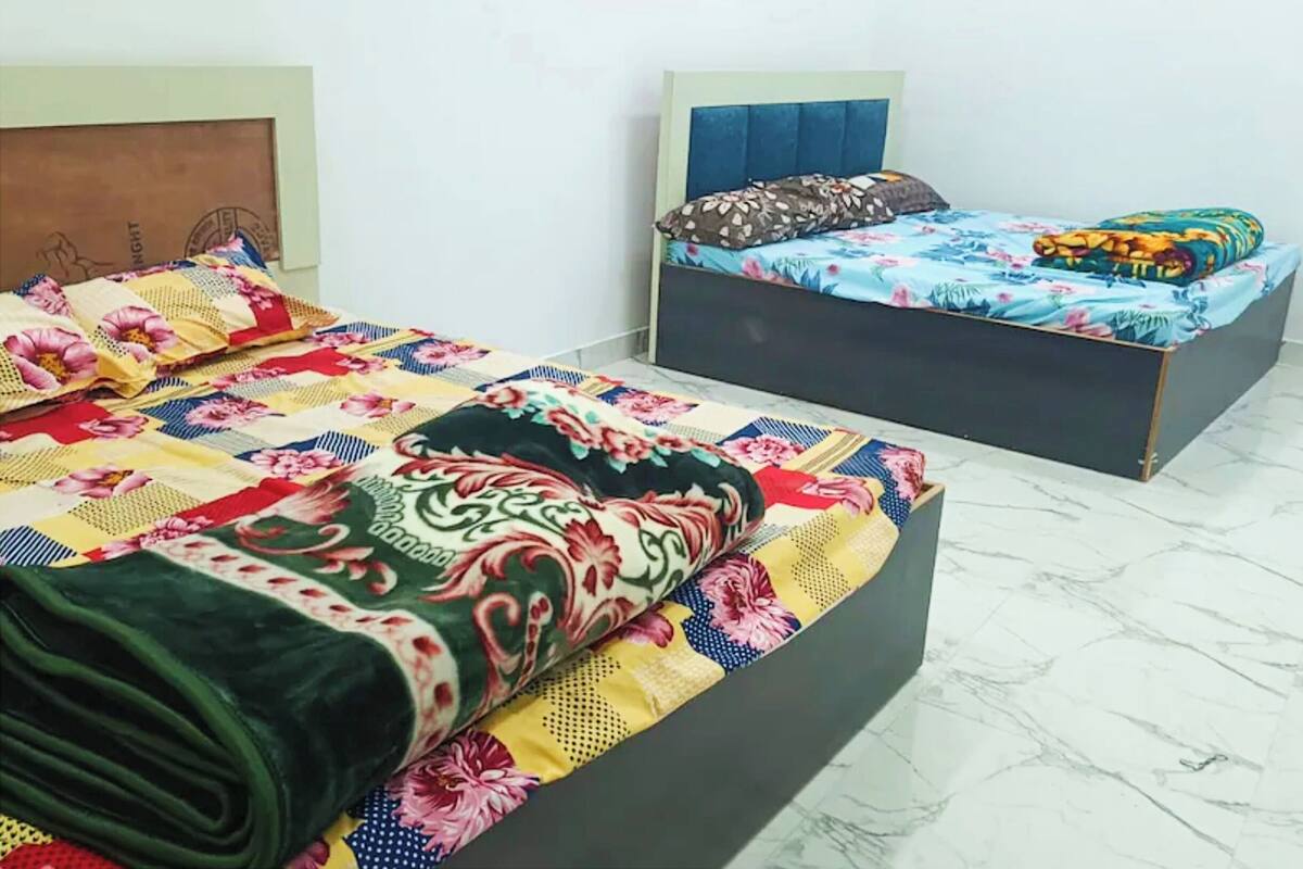 Habitación de hotel con dos camas, cada una con una colcha floral diferente. El piso es de mármol y el diseño es sencillo y moderno.