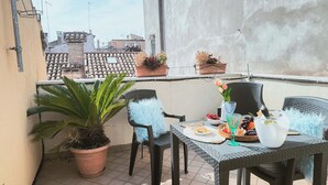 Un balcón con una mesa lista para dos personas, plantas en macetas y vistas de la ciudad.
