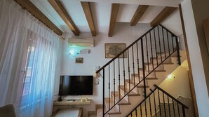Una sala de estar con una televisión de pantalla plana, vigas de madera, una escalera con barandillas negras y un mapa en la pared.