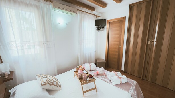 Un dormitorio con cama, mesita de noche, cortinas, un armario de madera y un pequeño taburete de madera con objetos encima.