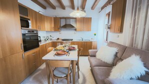 Una cocina compacta con armarios de madera, una mesa de comedor preparada para cuatro personas y un sofá con almohadones mullidos.