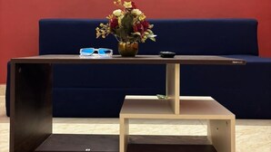 Een kamer met een donker houten salontafel, een klein krukje, een blauwe bank en een aan de muur bevestigd fotolijstje.