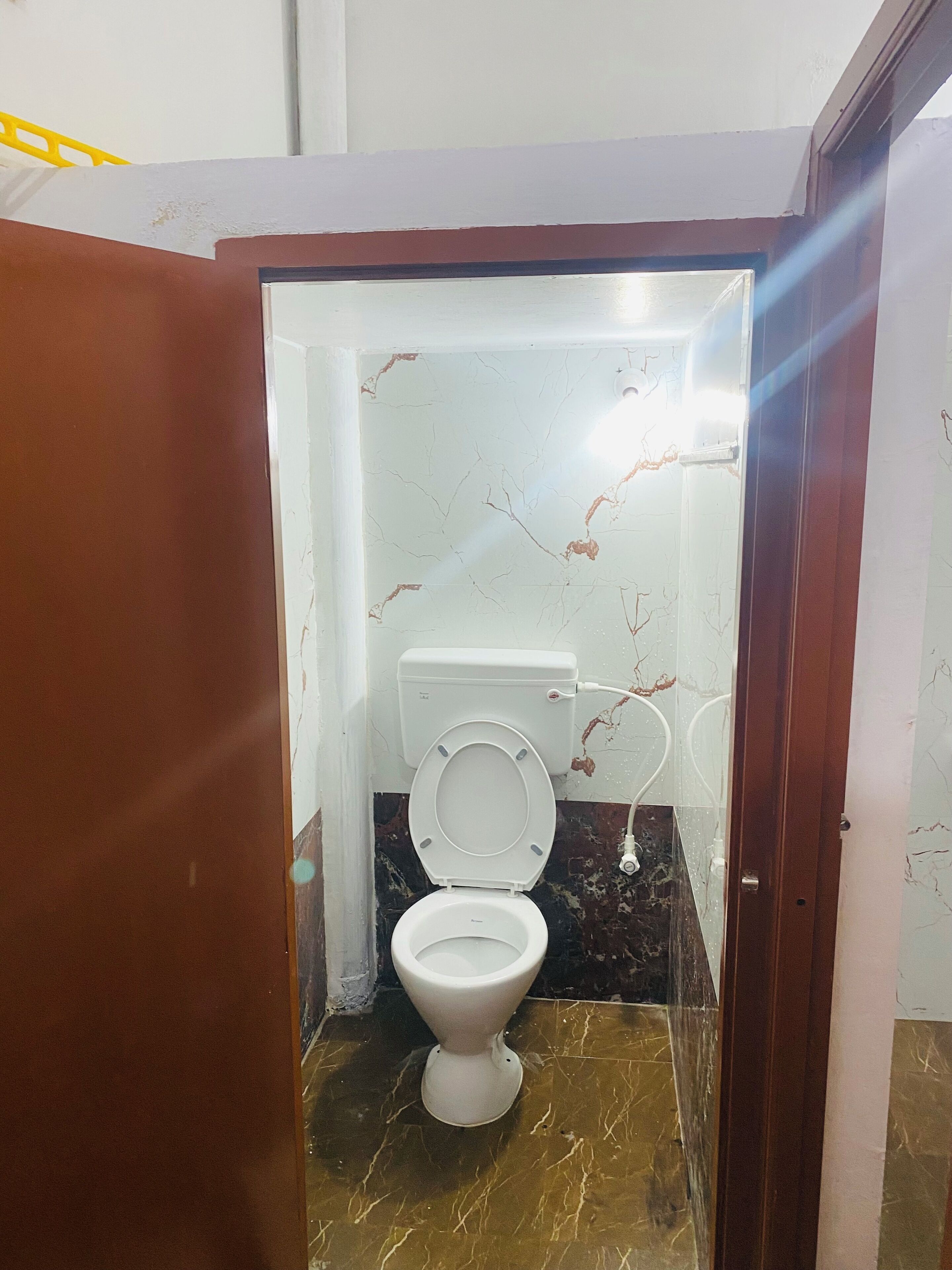 Un baño pequeño con inodoro, piso de mármol y pared blanca con una grieta.