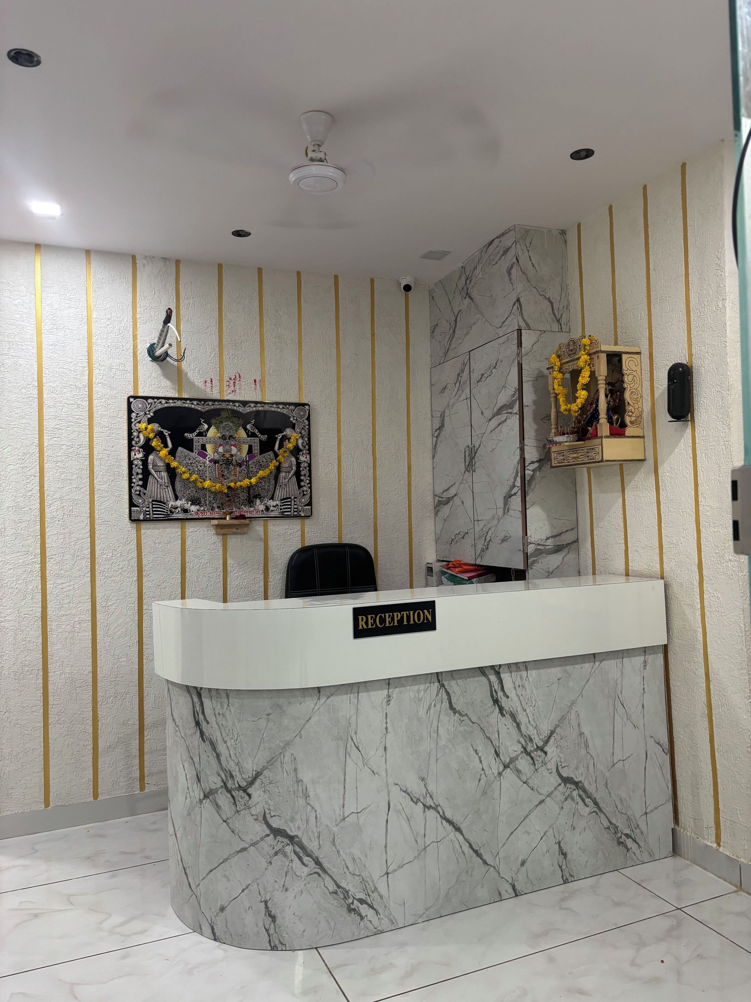 Un mostrador de recepción con base de mármol, una obra de arte enmarcada encima y un pequeño altar con flores.