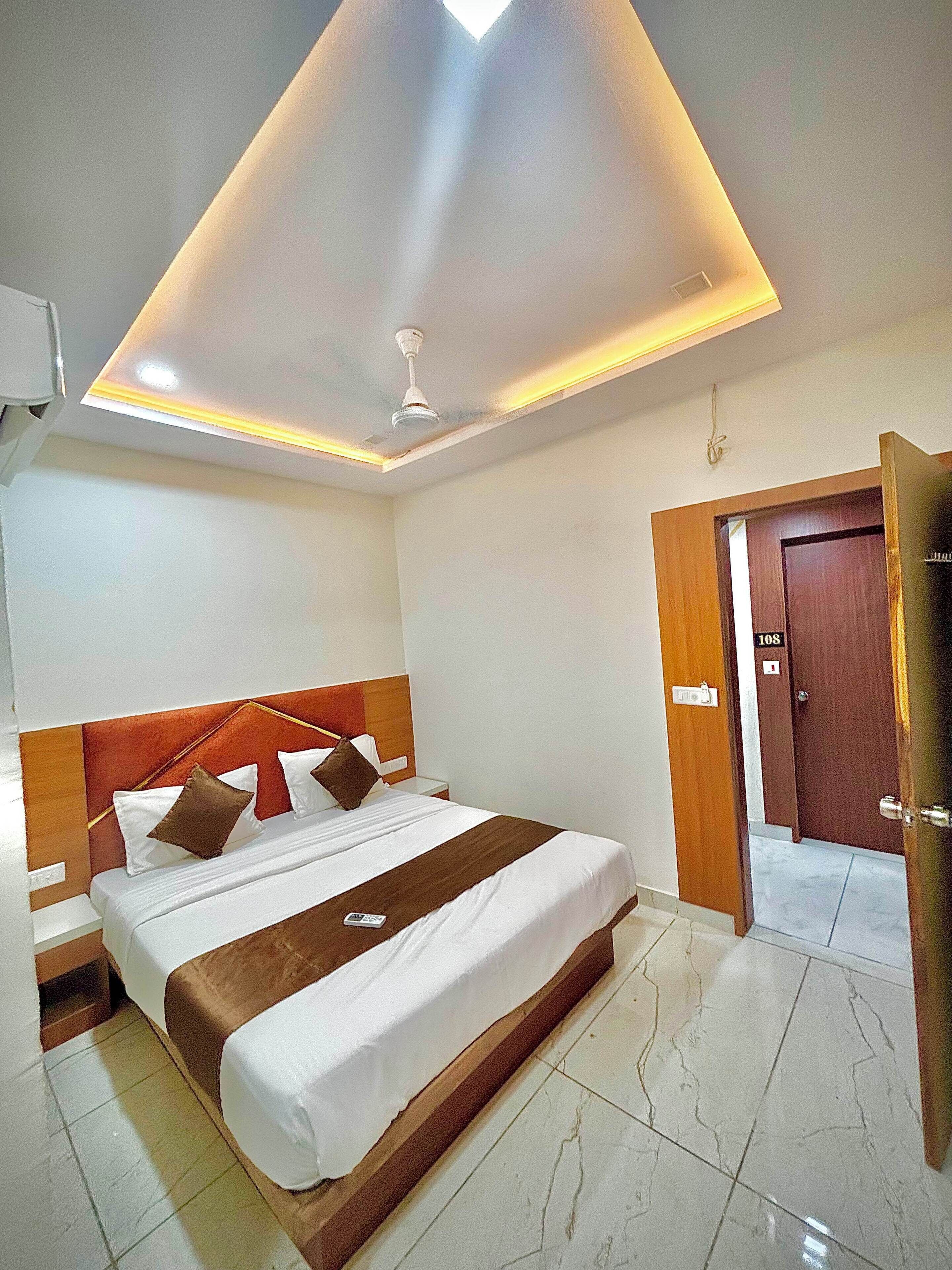 A hotel room with a bed, a ceiling fan, a door, and a light fixture.