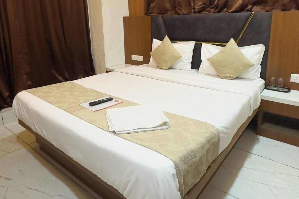 Une chambre d’hôtel avec un grand lit, une table de chevet, une commode, un ventilateur de plafond et une fenêtre avec des rideaux.