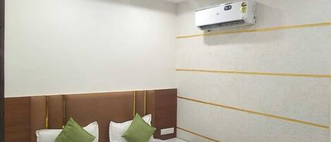Una habitación de hotel con cama, mesita de noche, aire acondicionado de pared y ventilador de techo.
