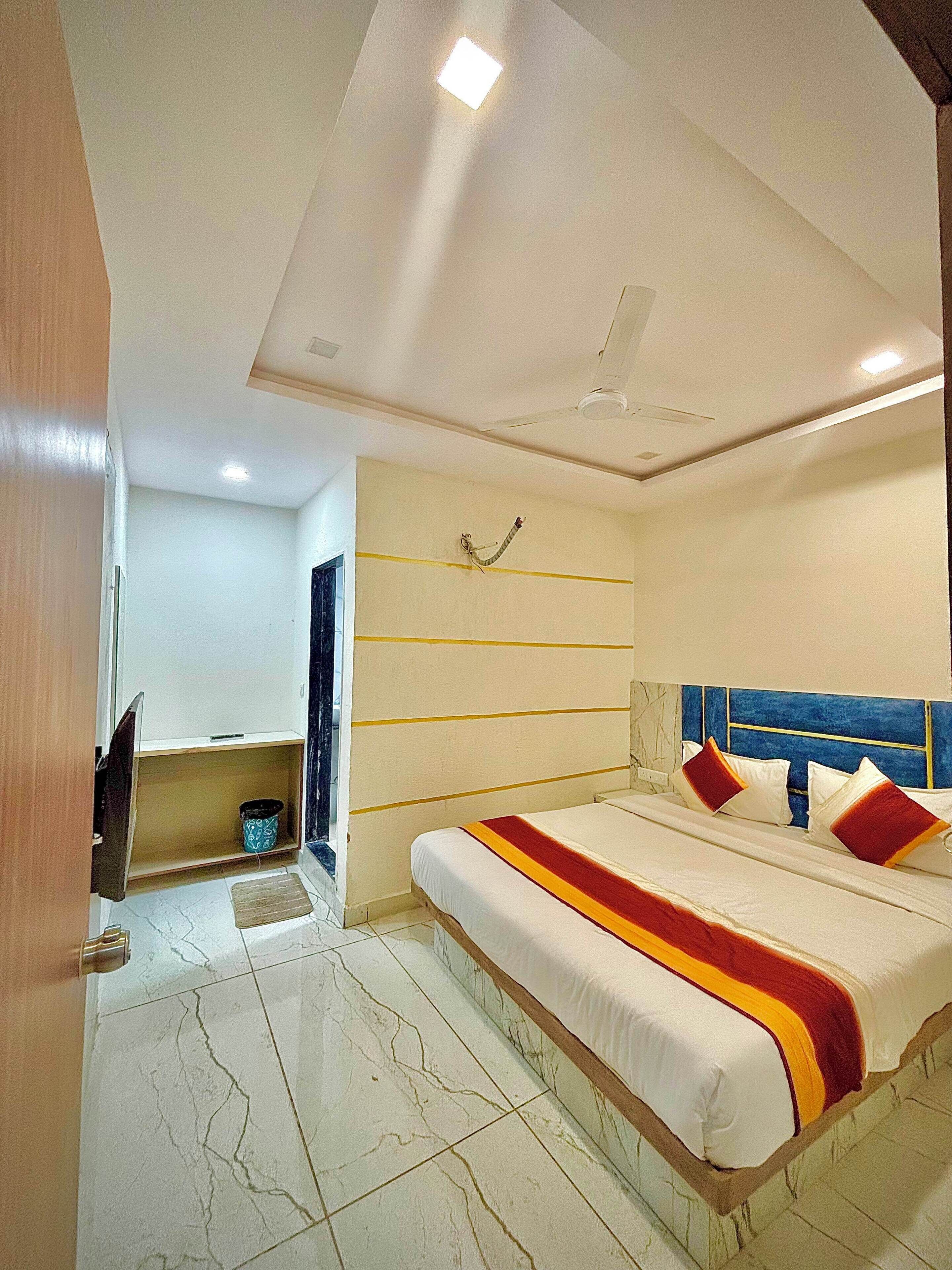 A modern bedroom with a large bed, a ceiling fan, and a small seating area with a TV.