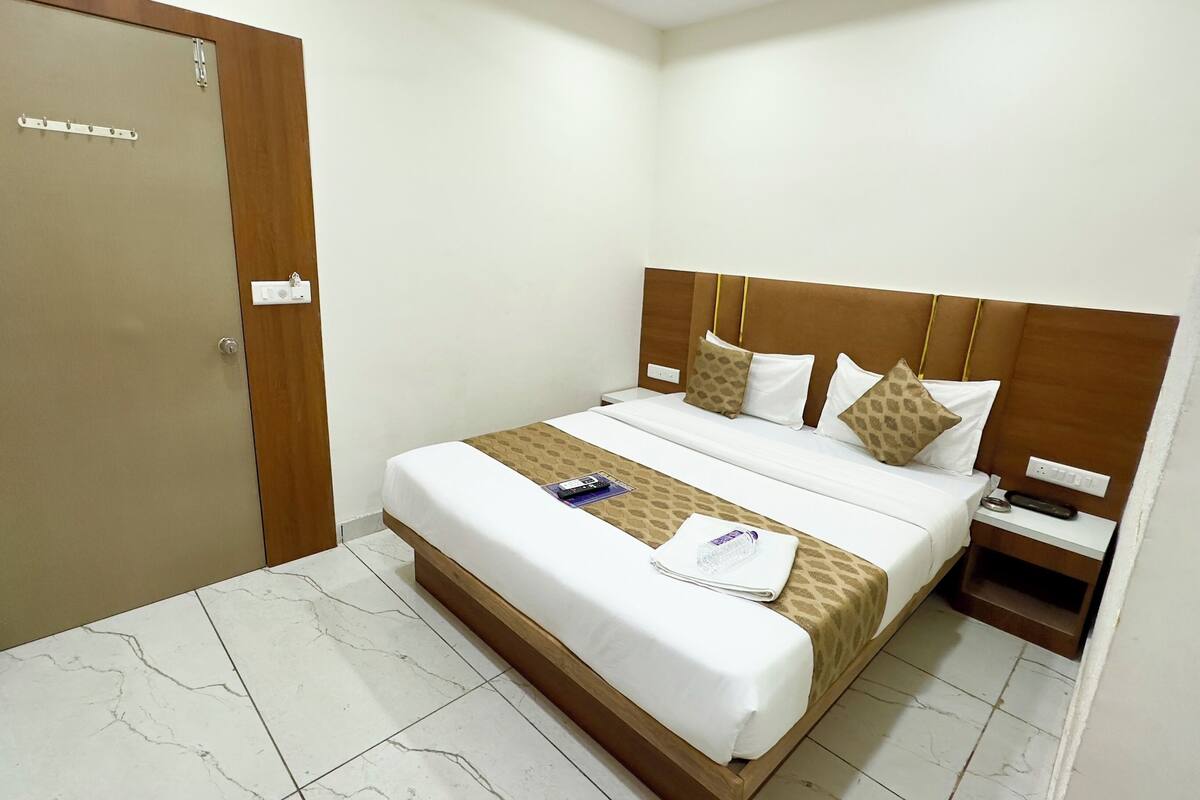 Une chambre d’hôtel avec un lit, une table de chevet, une porte en bois et un sol carrelé de carreaux blancs.