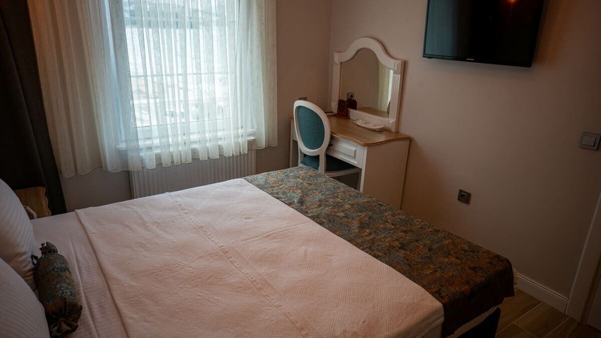 Un dormitorio con una cama, un escritorio con silla, un televisor y una ventana con cortinas.