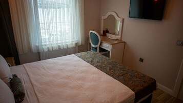 Un dormitorio con una cama, un escritorio con silla, un televisor y una ventana con cortinas.