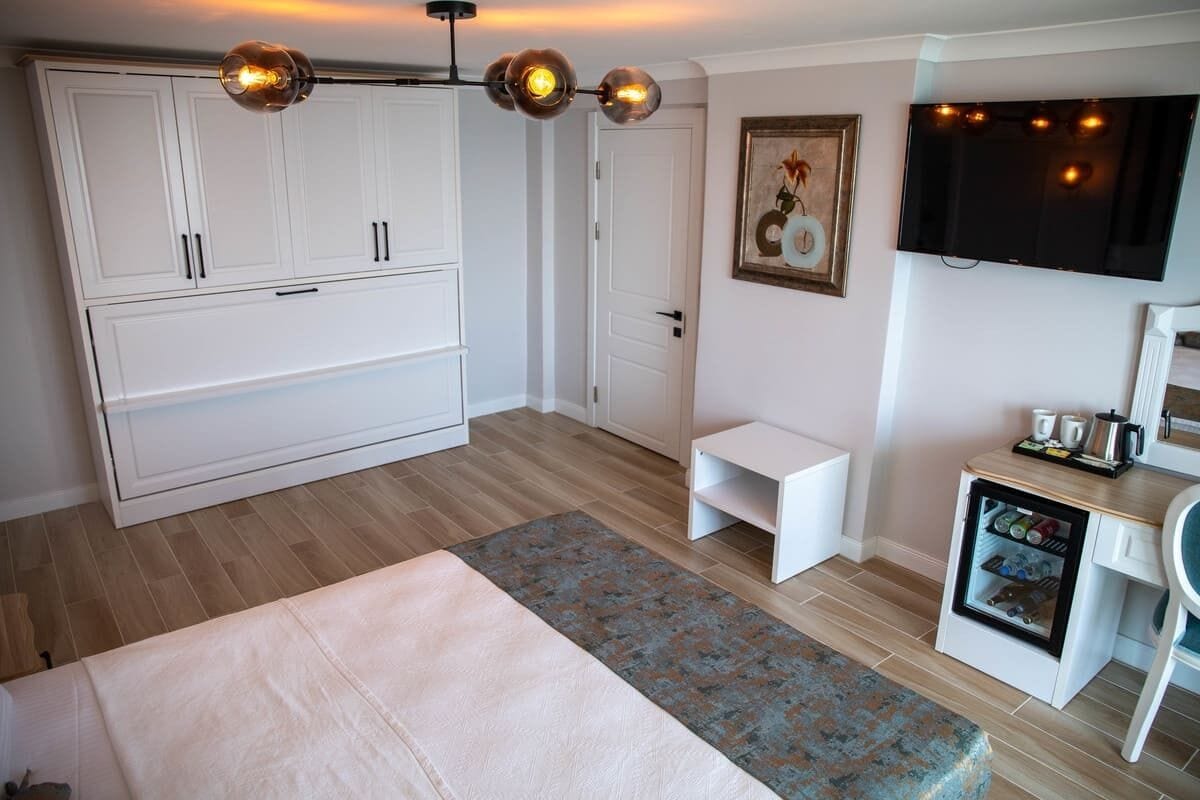 A bedroom with a bed, wardrobe, desk, television, and a mini-fridge.