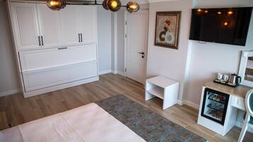 A bedroom with a bed, wardrobe, desk, television, and a mini-fridge.